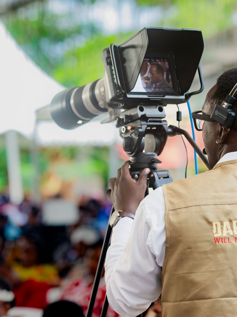 Camera operator with a headset filming an outdoor event with a long broadcast lens